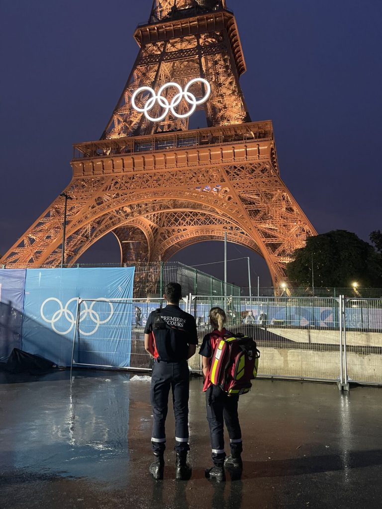 Deux secouristes face à la Tour Eiffel arborant les anneaux olympiques